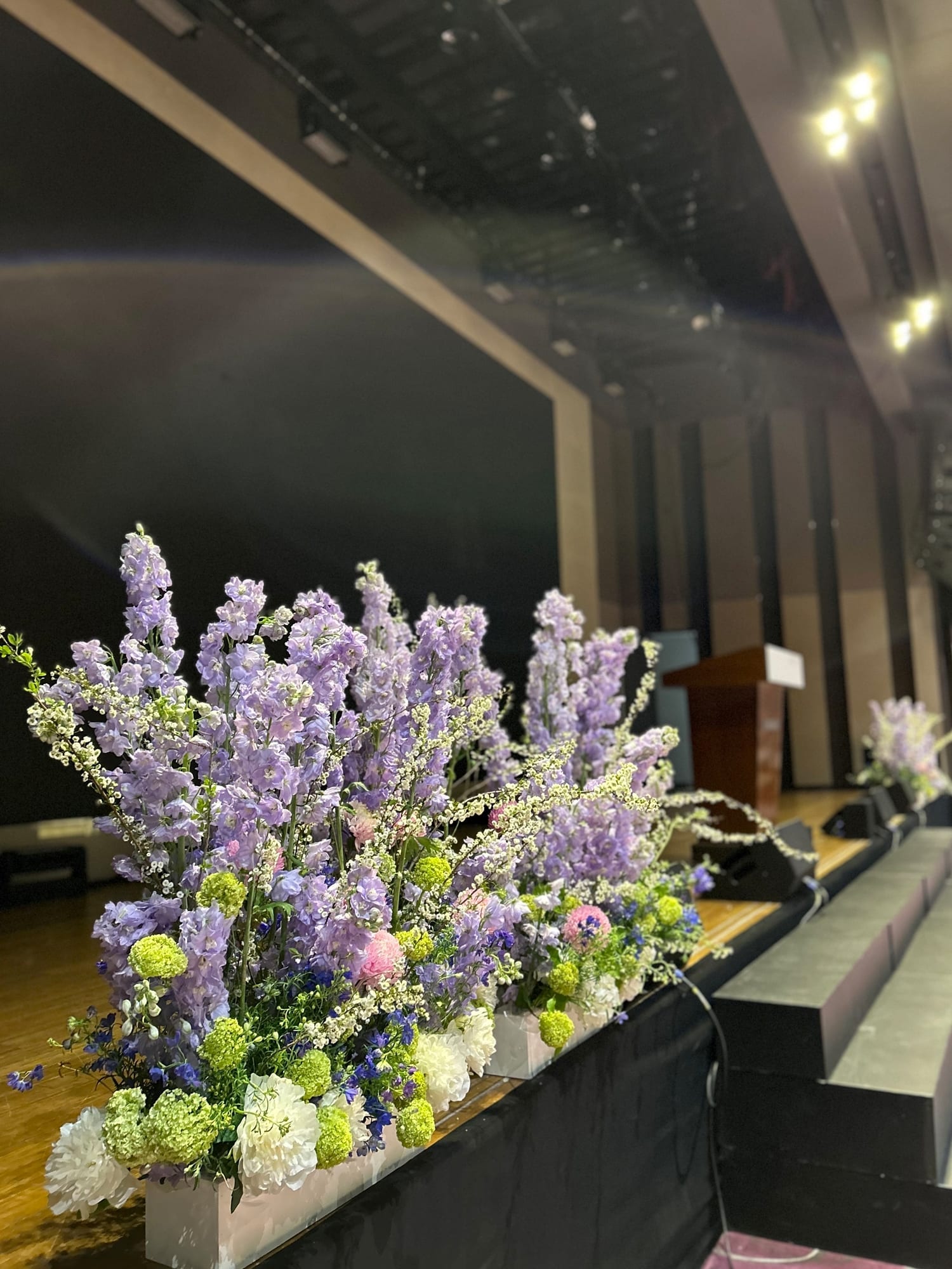 고양시 소노캄 행사장 — 무대 앞 단상을 따라 연보라·흰색 꽃을 길게 배치해 귀빈석을 장식한 모습
