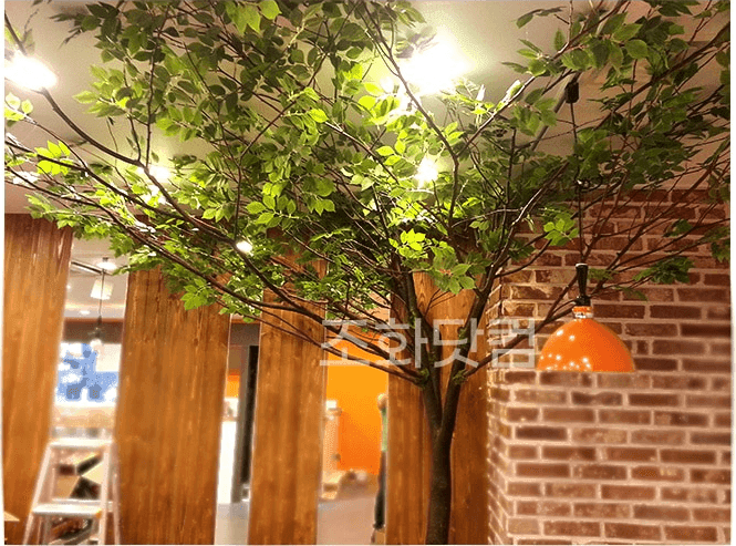 서울시 여의도 조PD 키친 — 노출 벽돌 벽을 따라 인조 느티나무 가지가 드리운 모습