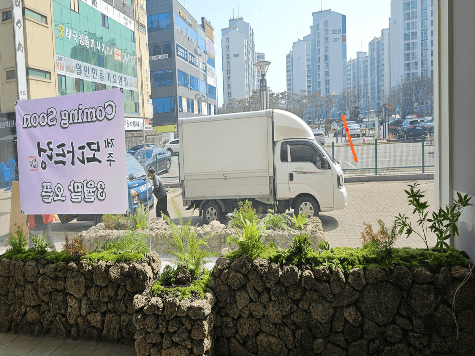 안산 모다드렁 — 오픈 준비 중인 실내에서 본 창가 돌담 화단과 거리 풍경