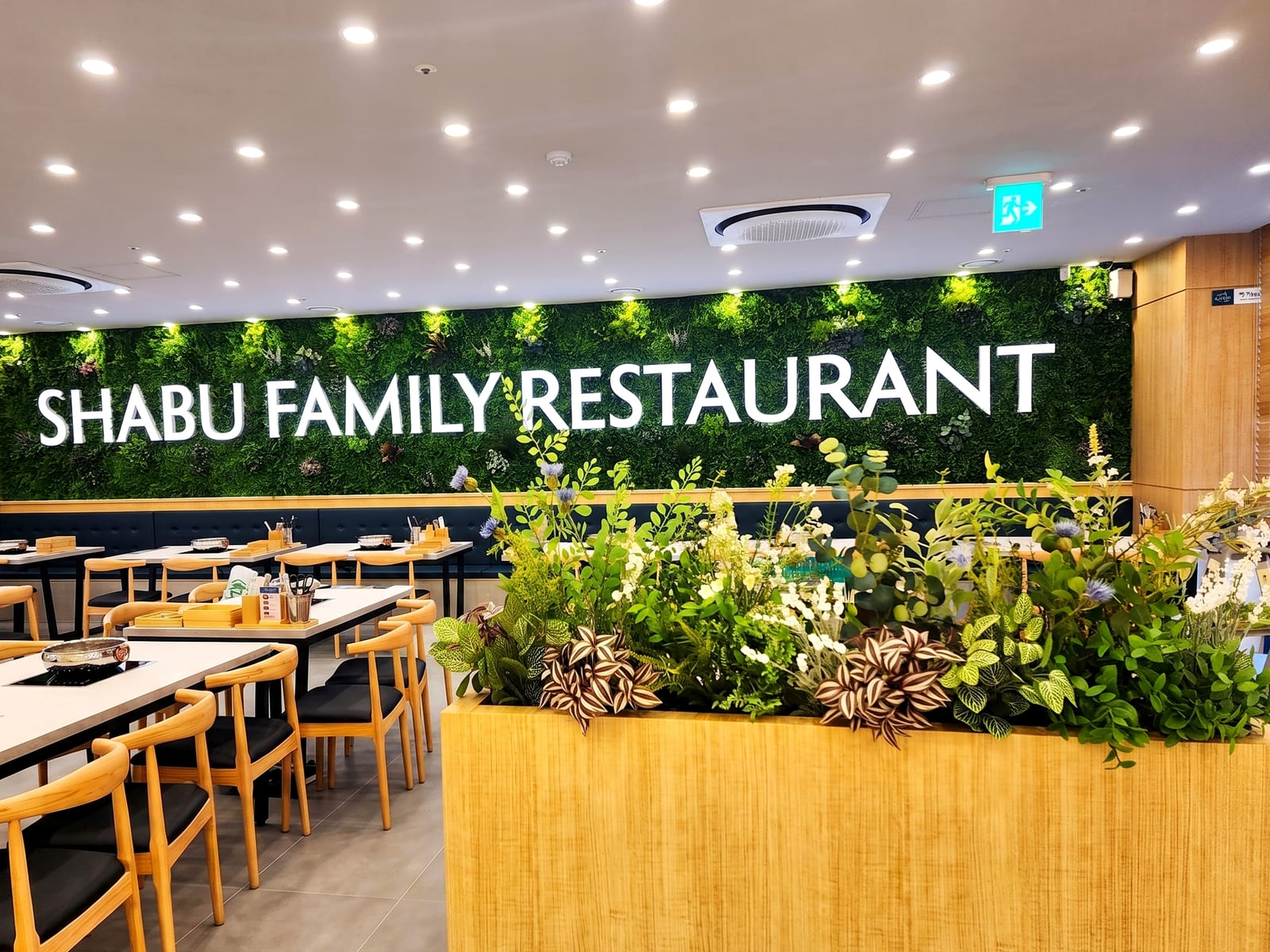 인천 샤브올데이 계산점 — SHABU FAMILY RESTAURANT 로고 배경 벽면을 인조 식물로 채운 벽면 녹화 그린월과 그 앞 플랜트박스