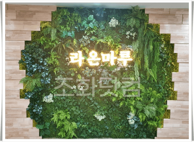 원주교육원 — 금색 기관명 사인 둘레를 여러 인조 식물로 액자처럼 둘러싼 벽면녹화