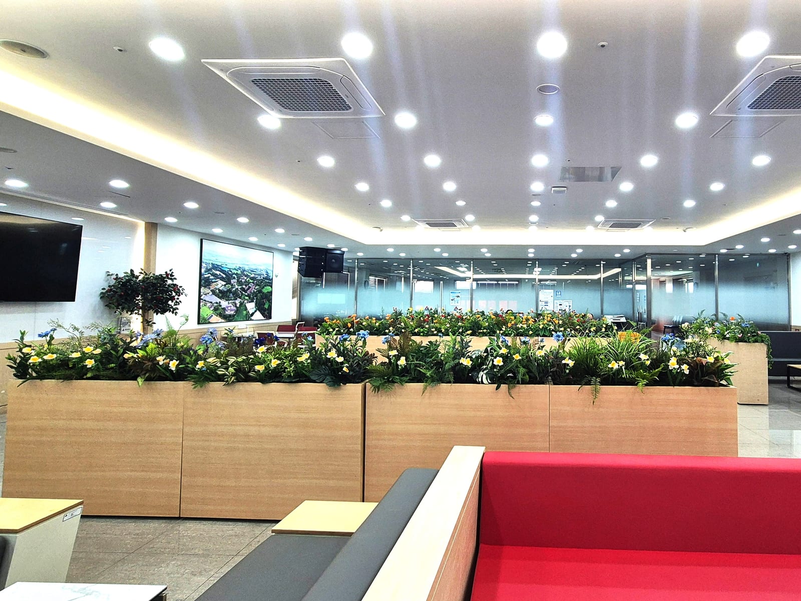 천안 연암대학교 — 붉은 소파가 있는 라운지를 가로지르는 컬러풀한 인조 꽃 플랜트박스